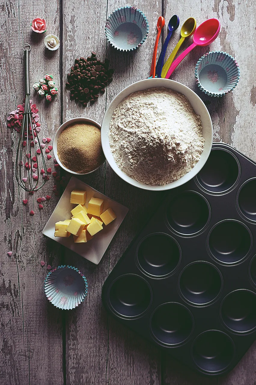 muffinspanna av kolstål, en skål med mjöl, färgglada måttskedar, pappersmuggar