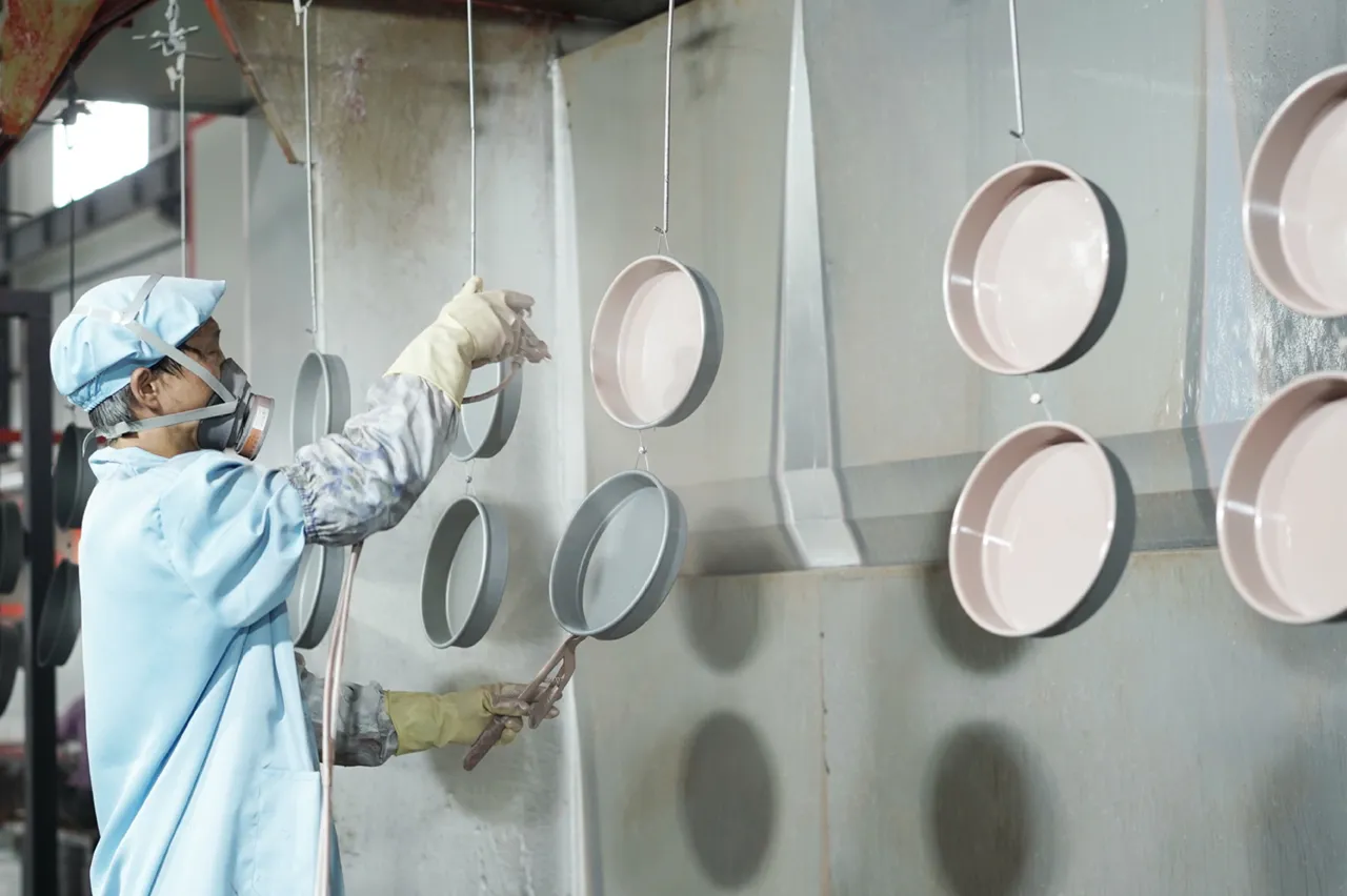 un muncitor profesionist care face pulverizare de acoperire antiaderență în fabrica de vase metalice de copt